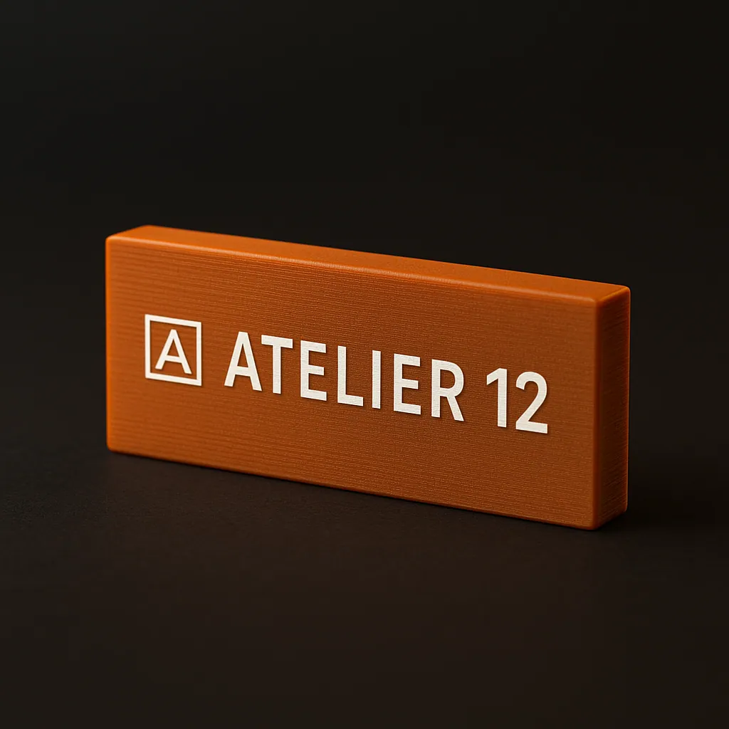 Orange 3D-printed nameplate laser-marked ATELIER 12 with a logo
